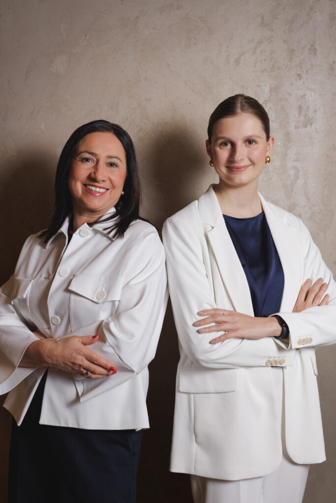 Zwei Frauen im professionellen Businessporträt stehen selbstbewusst nebeneinander vor neutralem Hintergrund